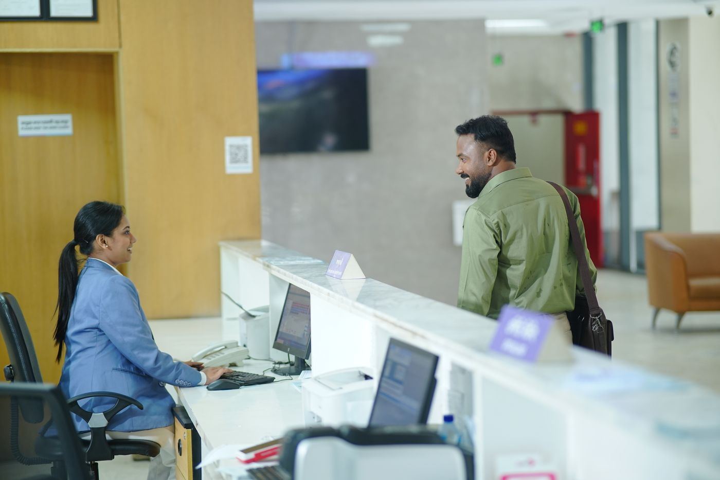 A receptionist at a computer as a visitor arrives